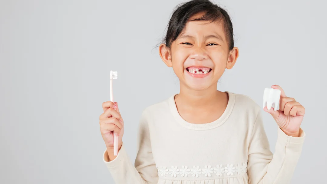 A young patient smiling at Dental Group of Aurora, holding a toothbrush and a model tooth